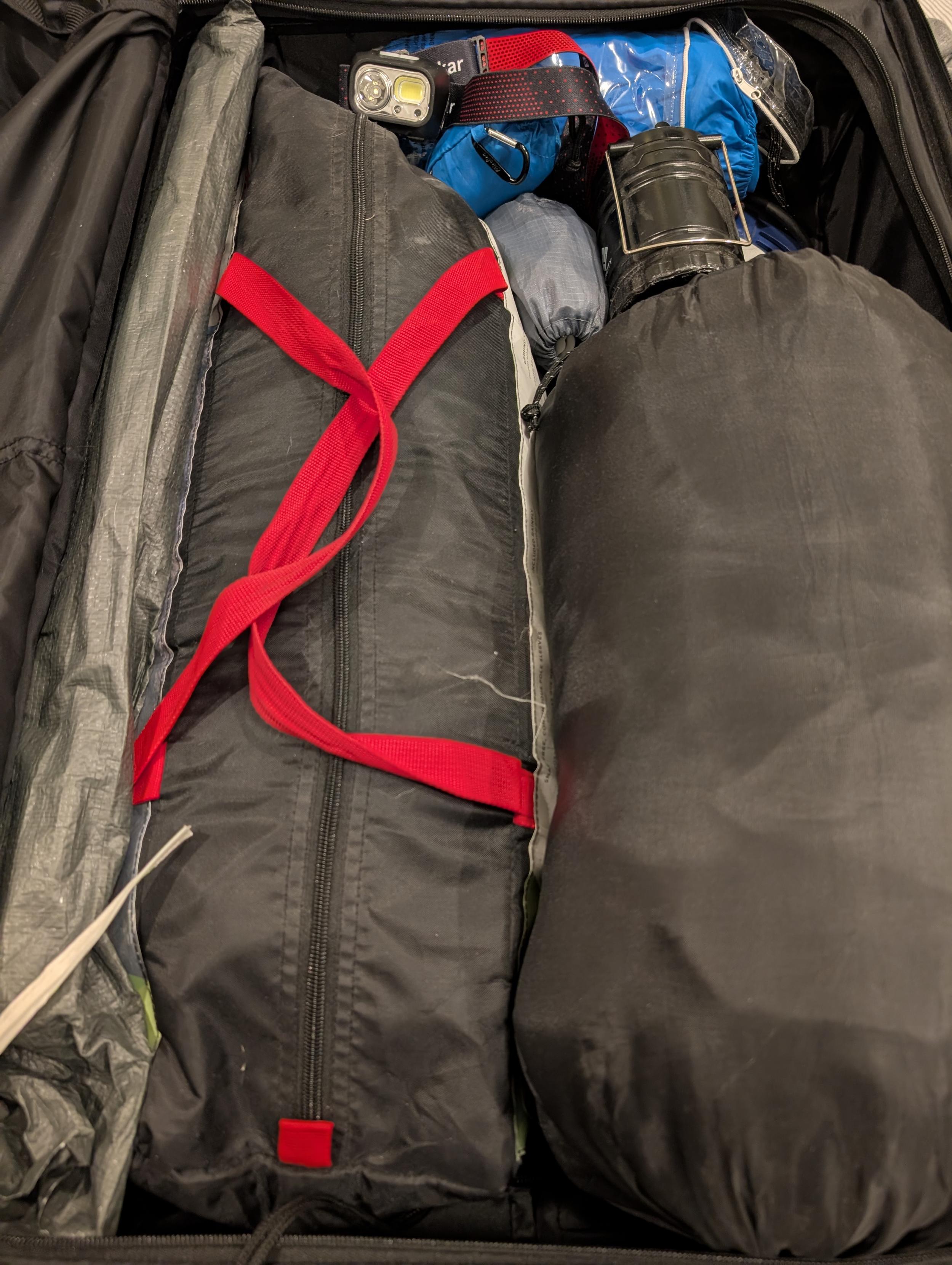 Suitcase containing a tent, some headlamps, a sleeping bag, other misc camping equipment, a British extension cord, a small battery powered lantern